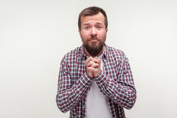 Please! Portrait of humble bearded young man in casual plaid shirt holding hands in prayer, looking...