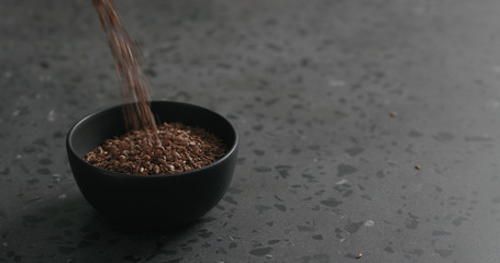 flaxseed falling into black bowl on terrazzo countertop