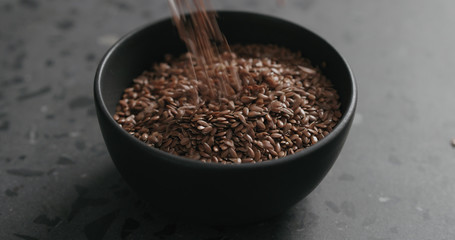 closeup flaxseed falling into black bowl on terrazzo countertop