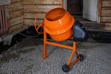 a small orange concrete mixer stands inside a wooden house for the manufacture of concrete floors