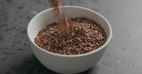 closeup flaxseed falling into white bowl on terrazzo countertop