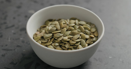 closeup pumpkin seeds in white bowl on terrazzo countertop