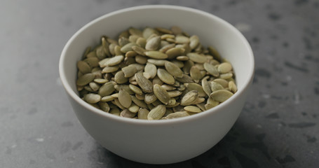 closeup pumpkin seeds in white bowl on terrazzo countertop