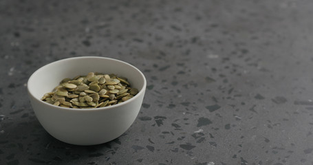 pumpkin seeds in white bowl on terrazzo countertop with copy space