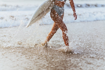 Surf girl with long hair go to surfing. Young surfer woman holding blank white short surfboard on a beach at sunset or sunrise.