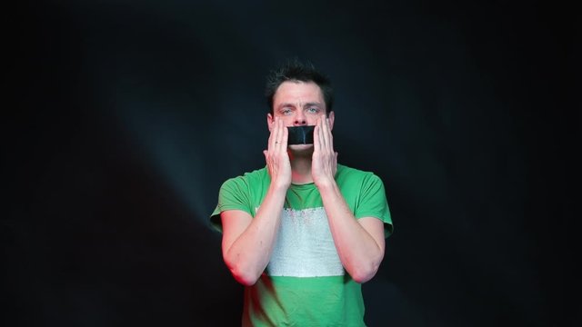 A man touches his face and lips taped with a black tape.