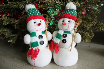 Two knitted Christmas snowmen in front of a Christmas tree.