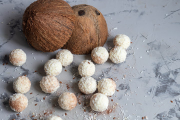 Candies in coconut flakes and fresh coconut with flax seeds on a gray stone background. Energy balls.