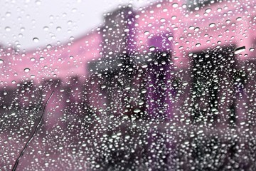 Water drops on window with blurred purple and black buildings in Background