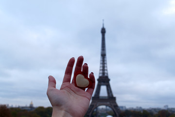 a woman's hand holds a red heart against the background of the Eiffel tower, in the most romantic city