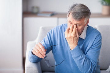 Elderly Man Massaging Nosebridge Sitting On Couch Indoor