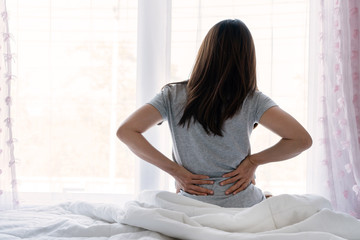 Sad young Asian woman touching back feeling backache morning discomfort low lumbar muscular kidney...