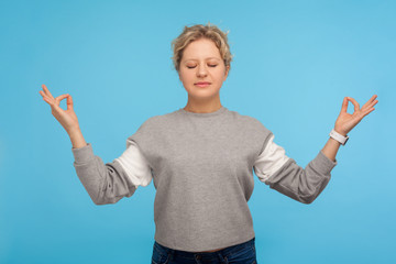 Harmony and balance. Tranquil woman with short curly hair in sweatshirt holding fingers in mudra...