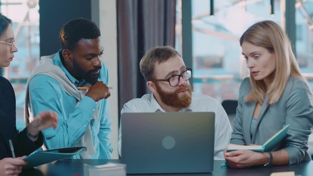 Group of multi-ethnic co-workers gathered together working discuss current issues common tasks, caucasian team leader talk with colleague business workplace skilled technology. Slow motion.