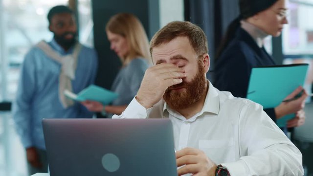 Feeling tired and stressed. Frustrated young redhair man keeping eyes closed and massaging while sitting at her working place in office. Young Businessman is tired and feels stressed out. Close up