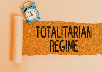 Writing note showing Totalitarian Regime. Business concept for mode of government that prohibits opposition parties Alarm clock and torn cardboard on a wooden classic table backdrop