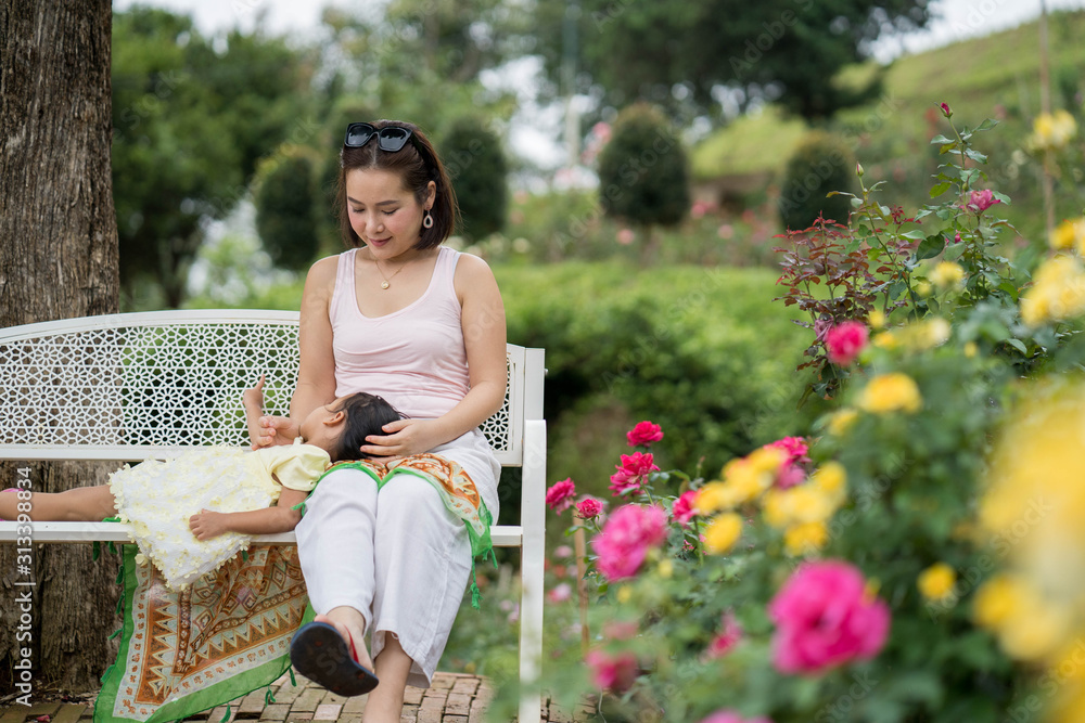 Wall mural Mum and daughter sitting on the bench at rose garden.