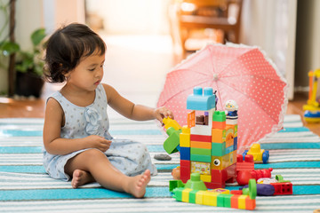 Cute asian girl playing plastic building blocks indoor.