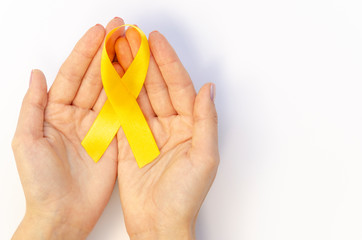 Close up top view hands holds Yellow gold ribbon on white table. Children cancer