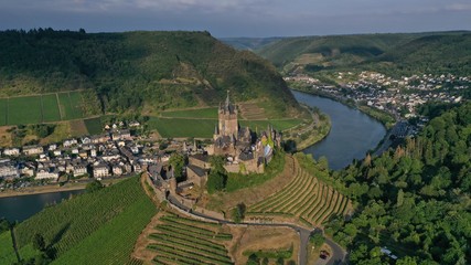 Aerial view of Cochem Castle on the hill near river surrounded by green vineyards, trees, fields, small houses, bridge. German flag waving on the top of tower. Summer. Germany historical landmarks.