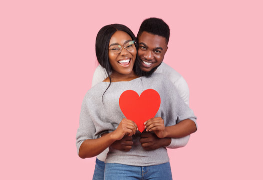 Joyful african couple holding big red heart together