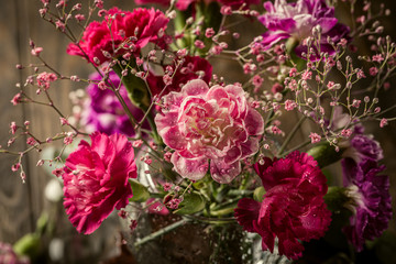 Bouquet of pink carnation in glass vase on old wooden background. Mothers day, birthday greeting card.