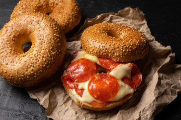 Sesame bagels with pepperoni and cheese on dark background