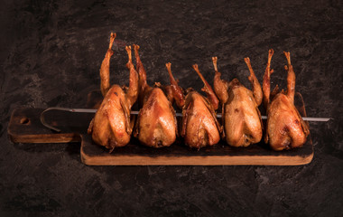 Roasted stuffed quail on a spit on a dark table.