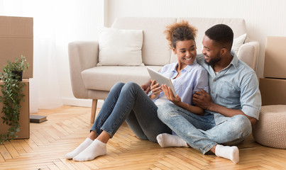 Joyful Black Spouses Using Tablet Computer Sitting On Floor Indoor