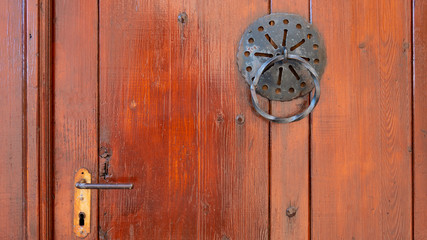 Old metal door handle knocker on a wooden door with handle.