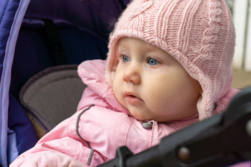 A little girl in a pink jacket in a pram looks around.