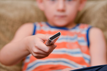 The boy on the couch switches the TV remote control.