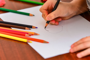 A girl draws a heart with colored pencils on a white sheet among children's toys.