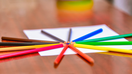 Color pencils lie on a blank white sheet on the table.