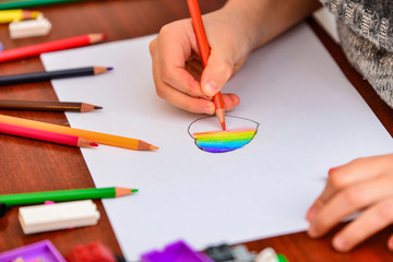 A girl draws a heart with colored pencils on a white sheet among children's toys.