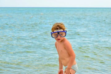 A boy with glasses for diving stands on the seashore.