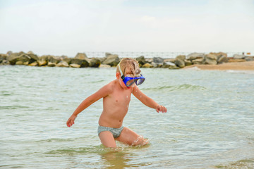 A boy with glasses for diving stands on the seashore.