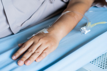 Obraz premium Patients saline, Iv drip, young woman hand with medical drip intravenous needle, give salt water on hospital bed. intravenous therapy (IV) is a therapy that delivers fluids directly into vein.