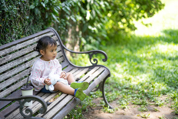 Cute little girl sitting at wooden bench in garden.