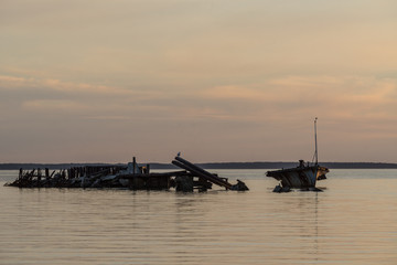 Fototapeta premium Old broken boat wreck on the shore, blue sea and sailboat on background. Harilaid, small island in Estonia, Europe.