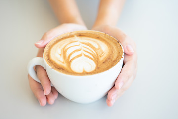 Woman hand holding a white coffee mug.  Coffee is a latte. table on the wooden table in vintage style, taken from the top view, see the froth of milk foam.