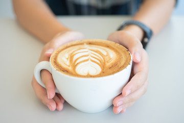 Woman hand holding a white coffee mug.  Coffee is a latte. table on the wooden table in vintage style, taken from the top view, see the froth of milk foam.