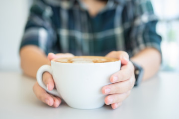 Woman hand holding a white coffee mug.  Coffee is a latte. table on the wooden table in vintage style, taken from the top view, see the froth of milk foam.