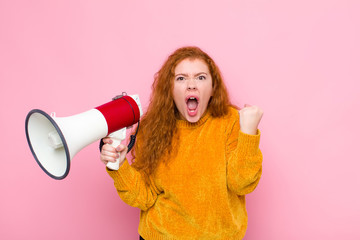 young red head woman shouting aggressively with an angry expression or with fists clenched...