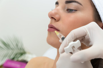 Powiększenie ust kwasem hialuronowym. Zbliżenie na usta kobiety podczas zabiegu modelowania ust. Kosmetolog wstrzykuje wypełniacz, medycyna estetyczna.  - obrazy, fototapety, plakaty