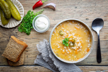 Soup with pickled cucumbers and pearl barley - rassolnik on wooden background, top view