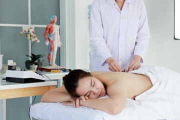 Fototapeta premium hand of doctor performing acupuncture therapy . Asian female undergoing acupuncture treatment with a line of fine needles inserted into the her body skin in clinic hospital