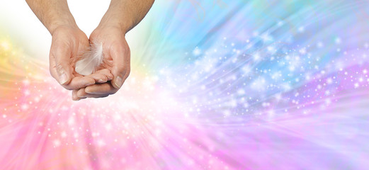 Gentle Angelic Healing Hands Message Banner - male cupped hands offering a white feather against a rainbow coloured sparkling flowing ethereal energy background with copy space