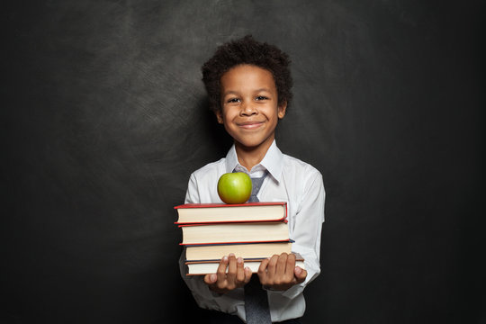 Happy black child student holding books and apple and smiling on chalkboard background