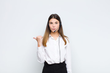 young pretty woman looking astonished in disbelief, pointing at object on the side and saying wow,...